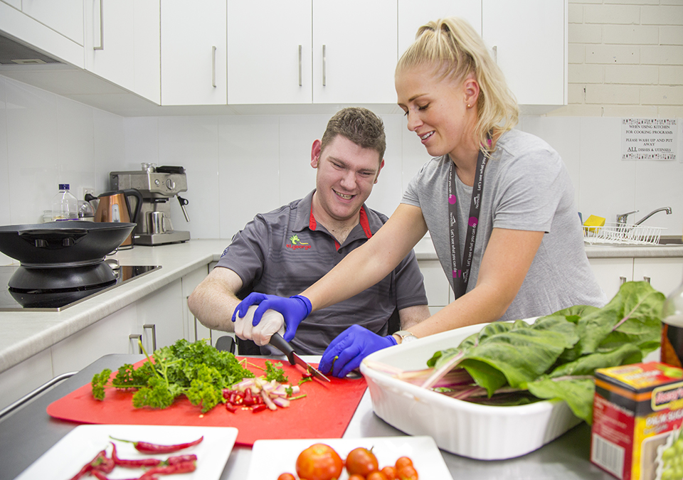 Man being supported to cut vegetables in a kitchen